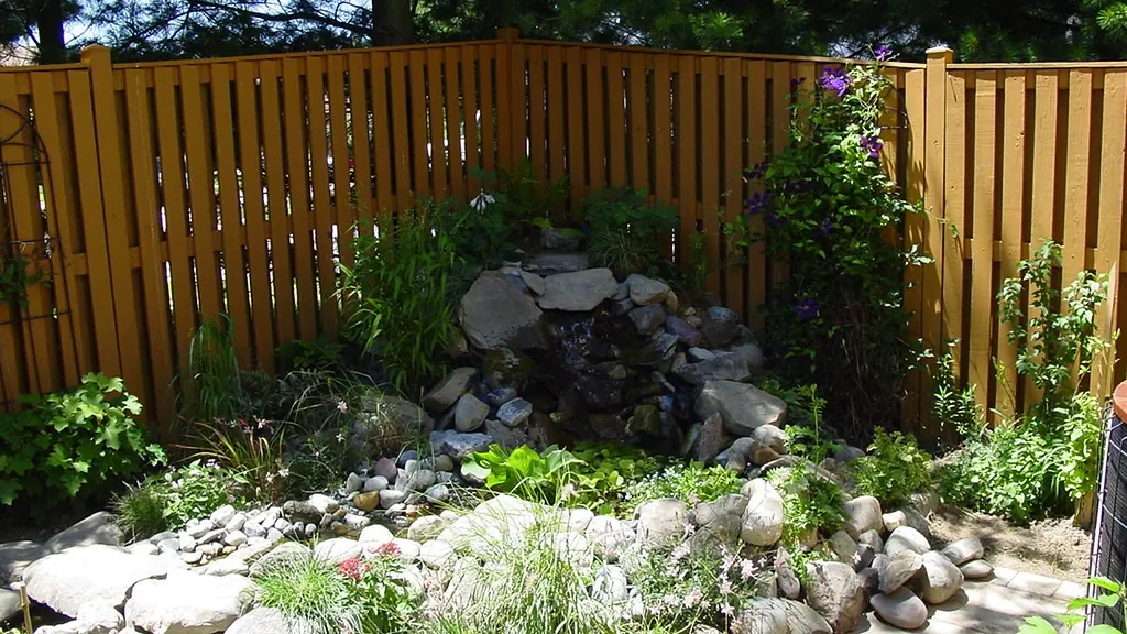 After: the same corner with a stone waterfall, pond, and new plantings